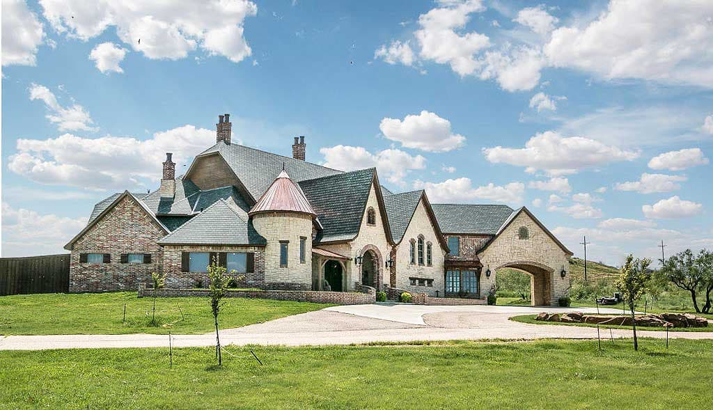 House plan exterior featuring a complex roofline, stone and brick facade, multiple gables, and a circular turret with a copper roof.