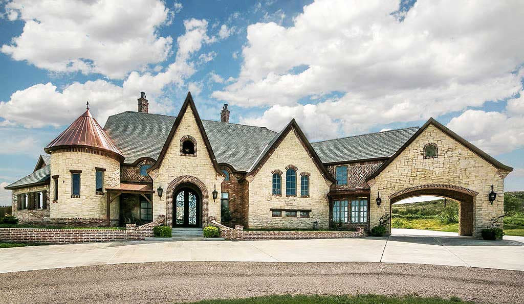 House plan exterior with stone and brick facade, multiple gables, arched entryway, and a porte-cochère.