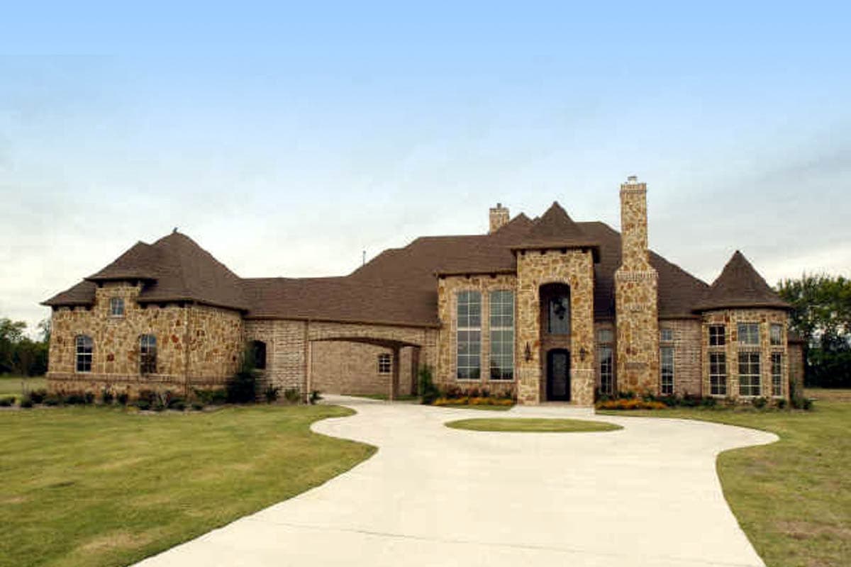House plan exterior with stone facade, arched windows, multiple gables, and porte-cochere.