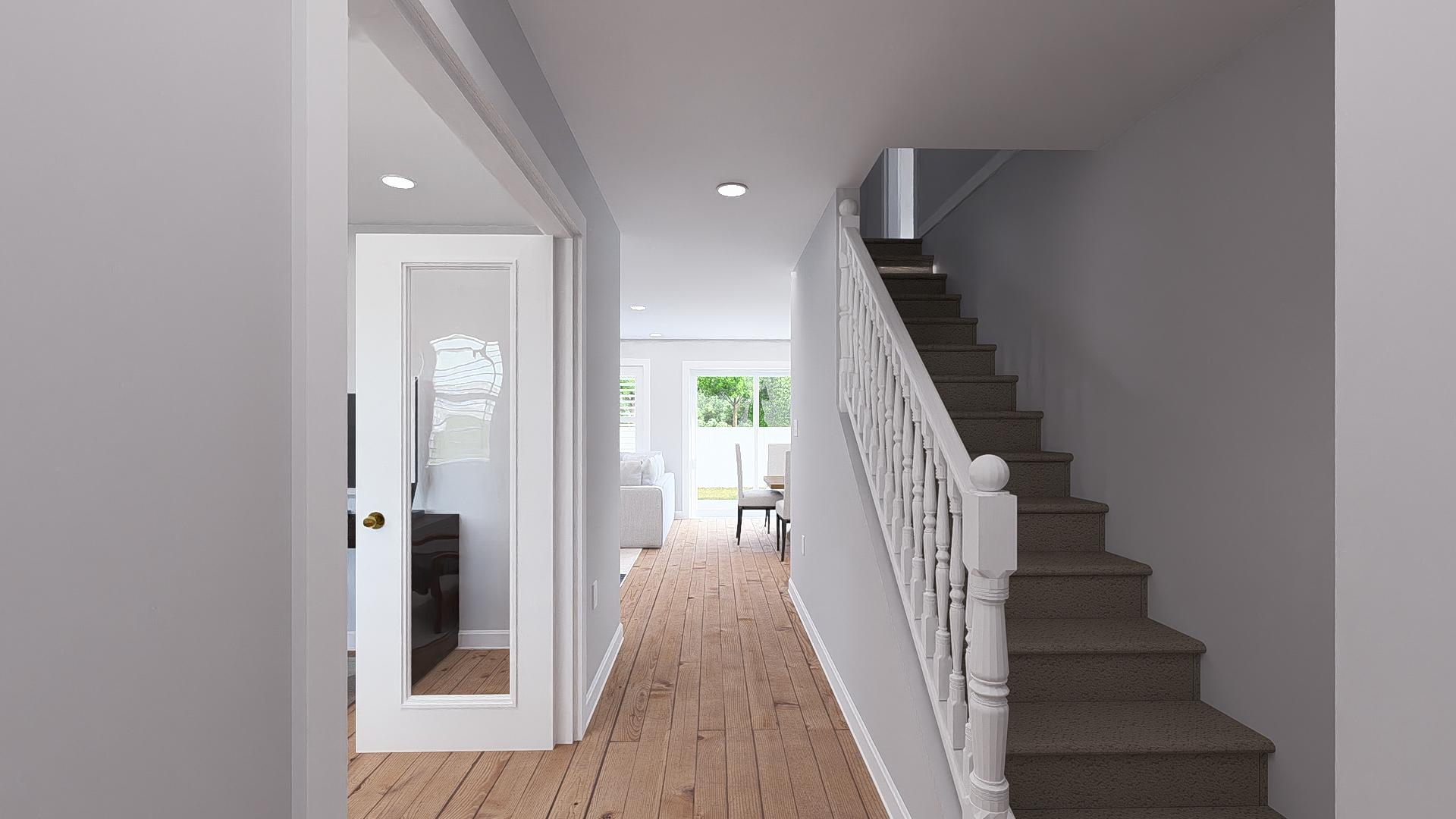 Interior view of a hallway with a staircase and doorway leading to a living and dining area.