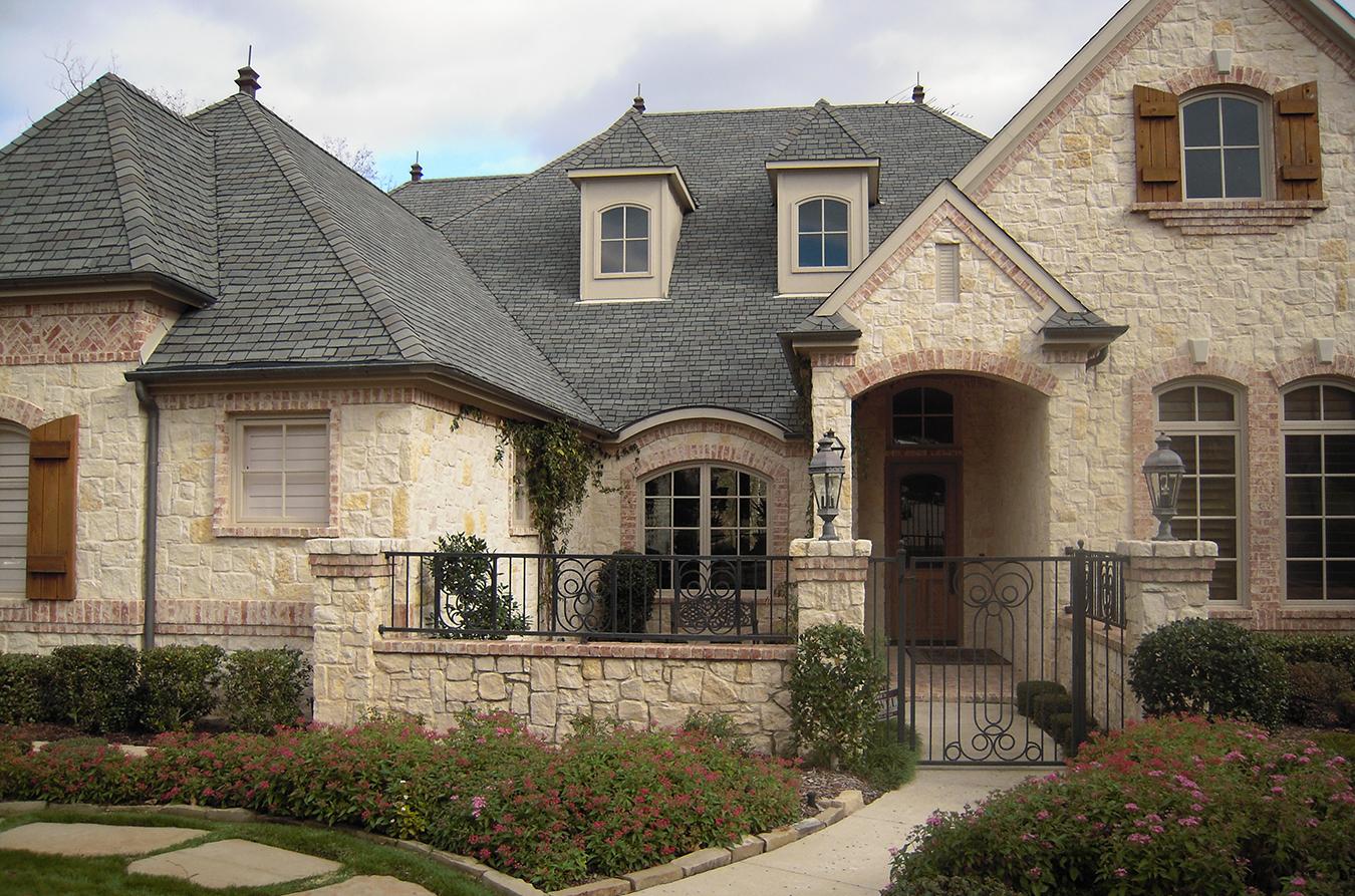 House plan exterior with stone and brick facade, dormer windows, arched entryway, and wrought iron fence.