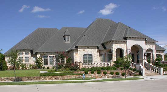 House plan exterior: One-story stone-clad residence with multiple gables, arched windows, a dormer, and an arched entry portico.