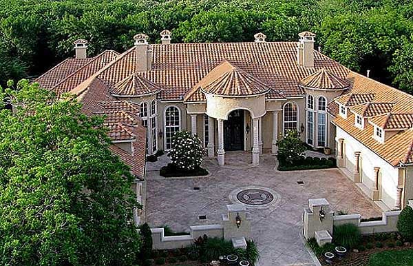 House plan exterior of a large, two-story Mediterranean-style home with a clay tile roof, multiple gables, arched windows, and a porte-cochère.