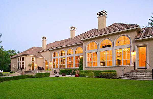 House plan exterior: expansive arched windows, multiple chimneys, and clay tile roof.