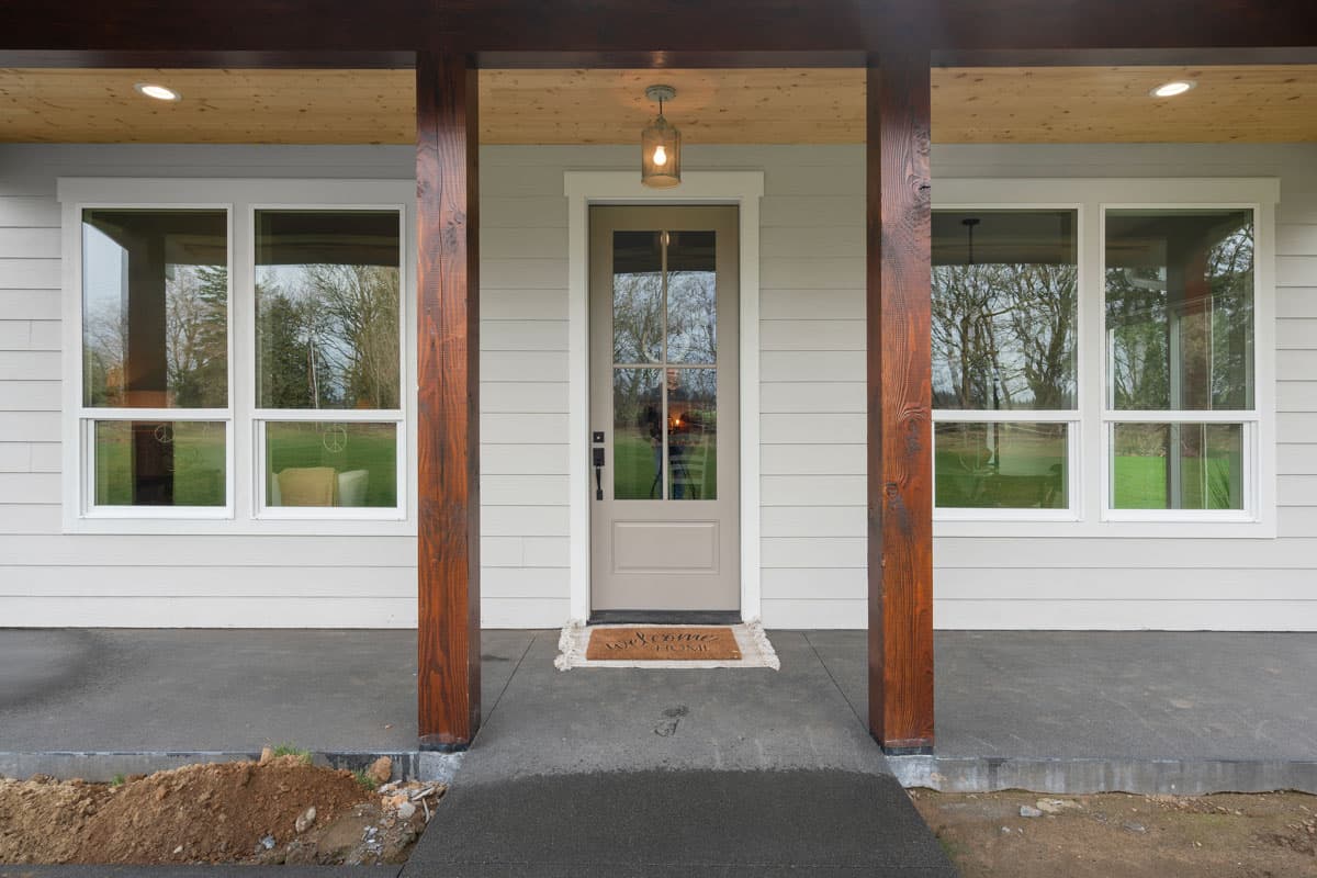 House plan exterior featuring a covered porch with wood posts, a glass-paneled door, and double-hung windows.