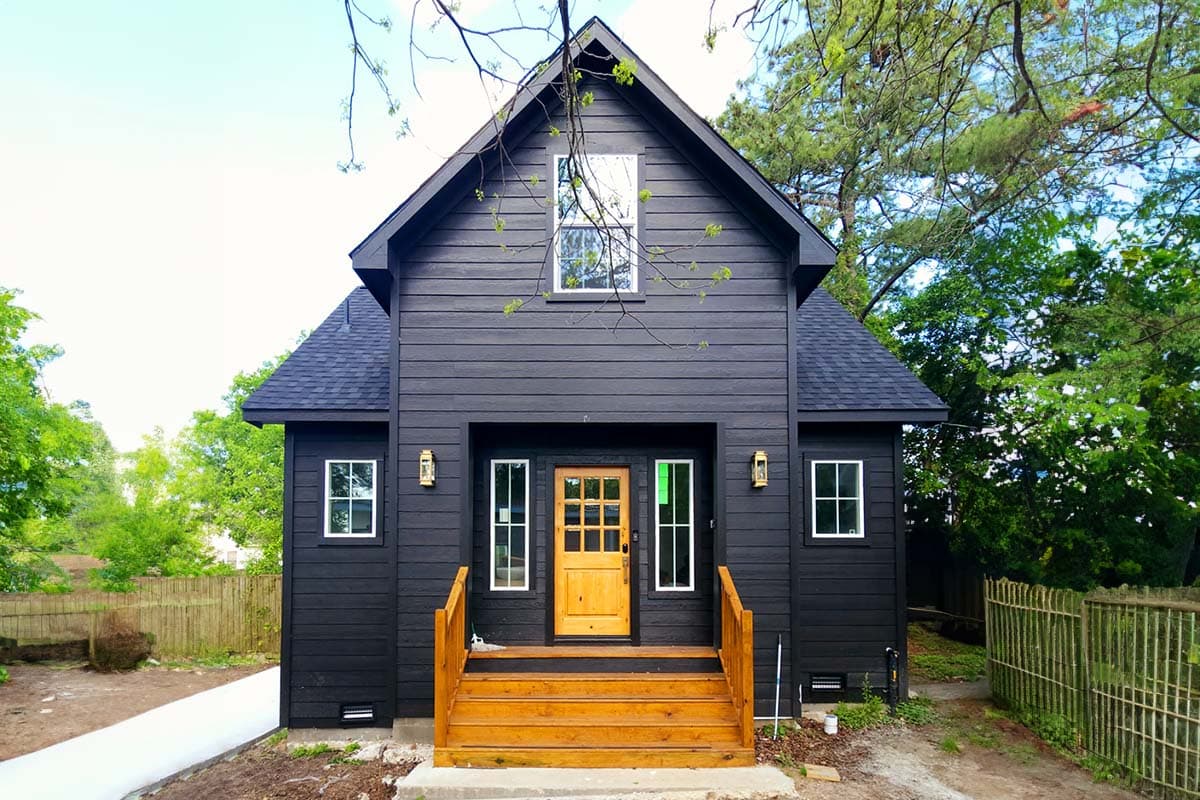 House plan exterior: Two-story modern home with dark horizontal siding, prominent gable, wood porch with yellow door, and white-framed windows.