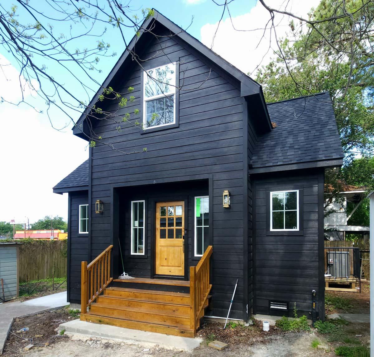 Modern two-story house plan exterior with black horizontal siding, wooden front door, multiple windows, and a prominent gable.