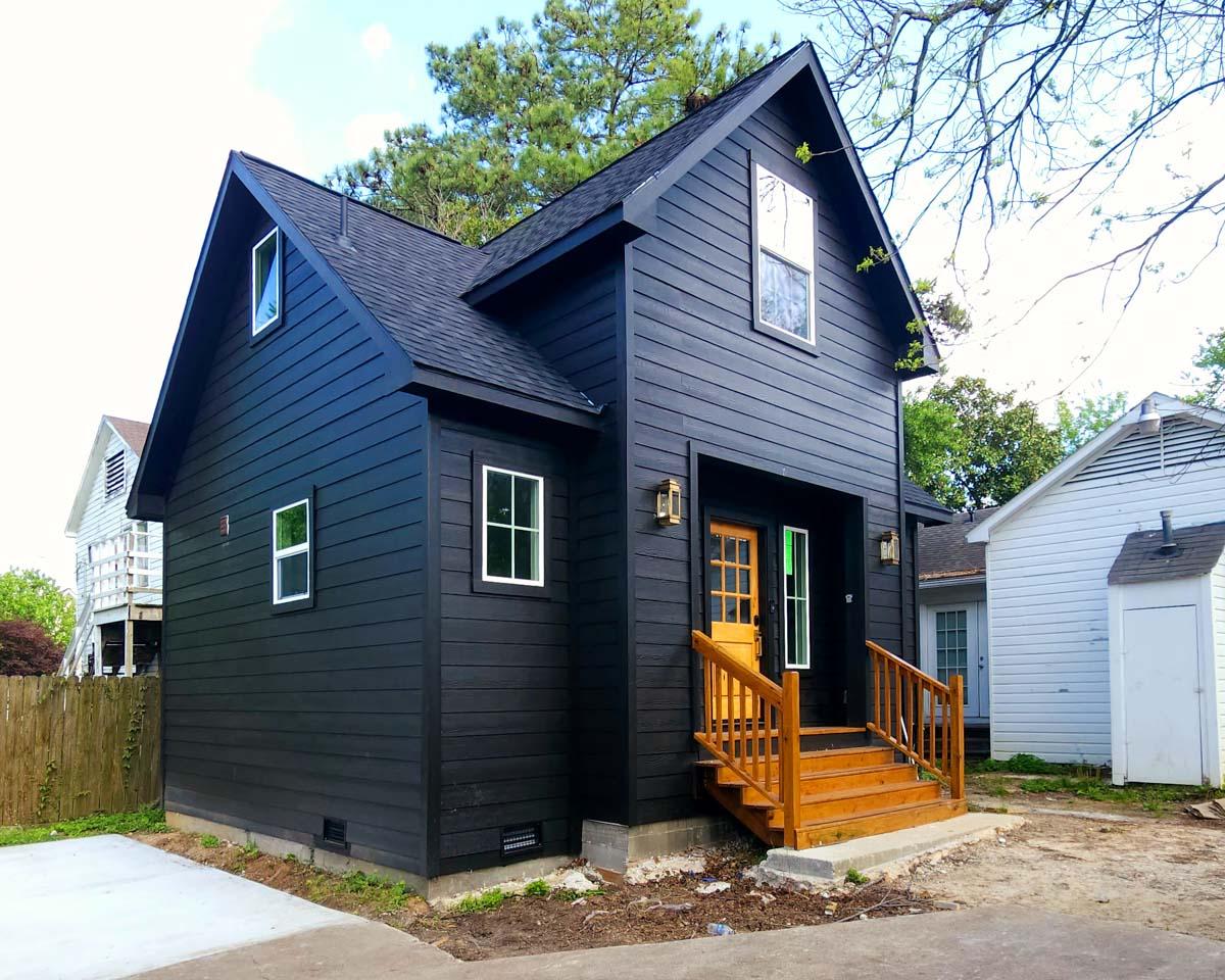 House plan exterior, two-story modern home with dark siding, prominent gable, wood porch steps, and double-hung windows.