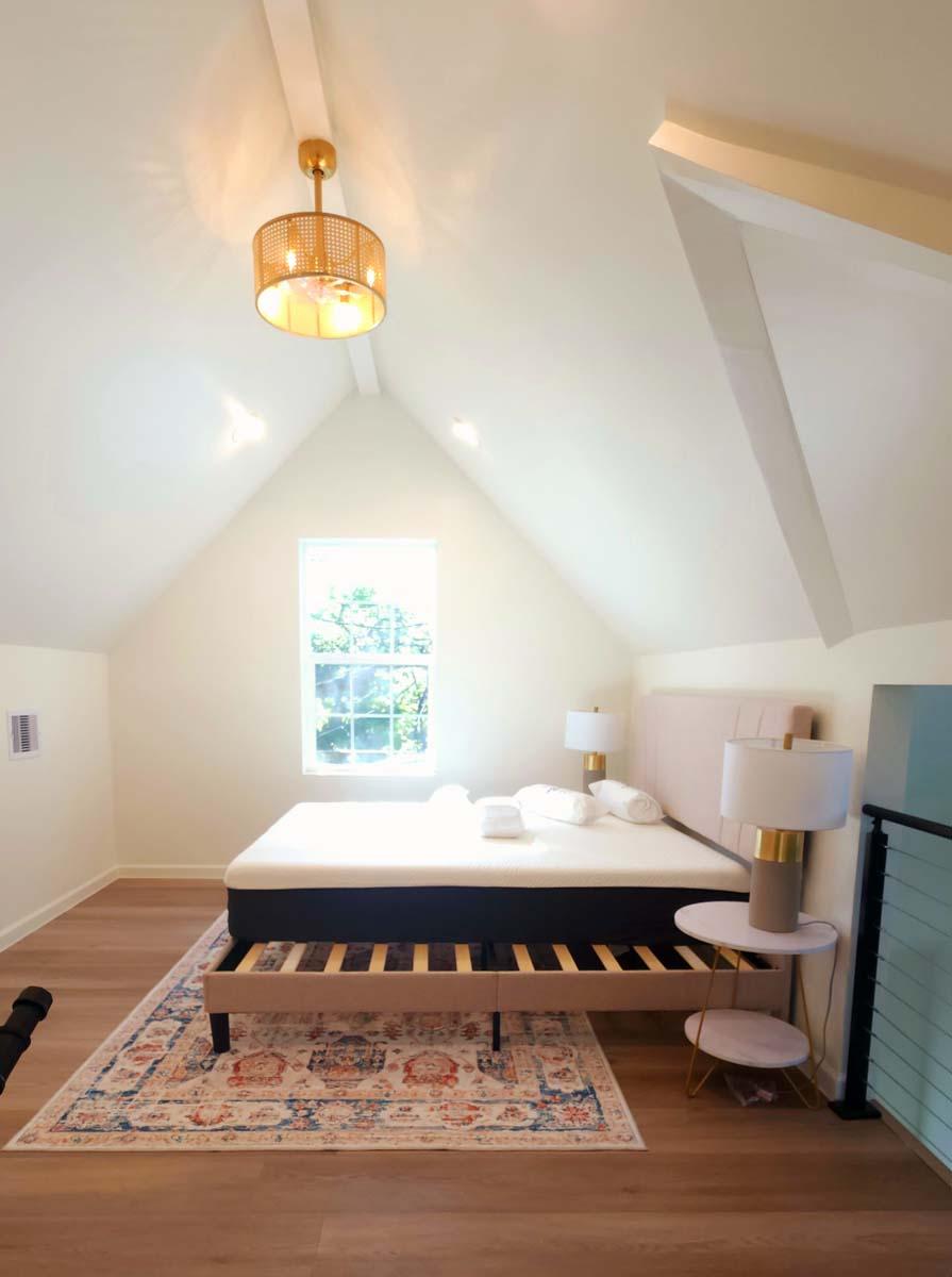 Bedroom with vaulted ceiling, king bed, window, and cane pendant light.
