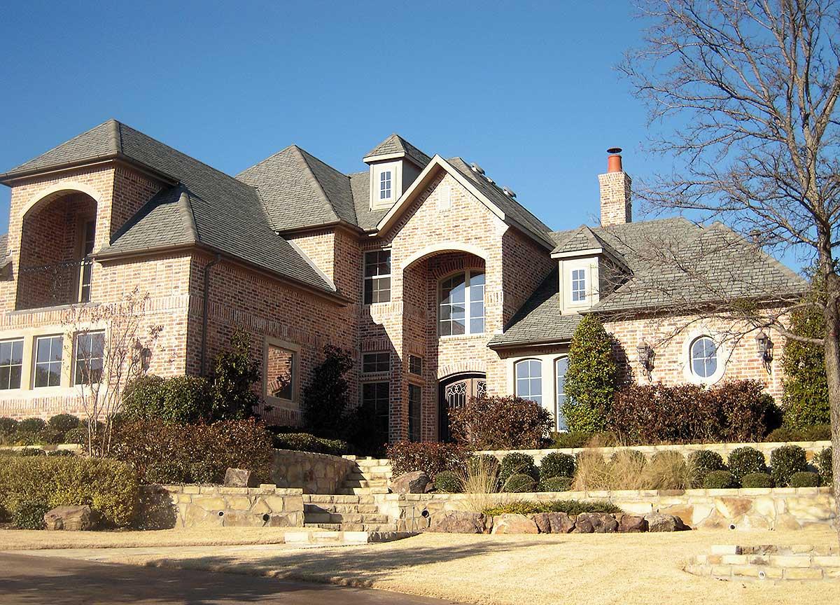 House plan exterior with brick facade, arched entryway, multiple gables, dormers, and a prominent chimney.