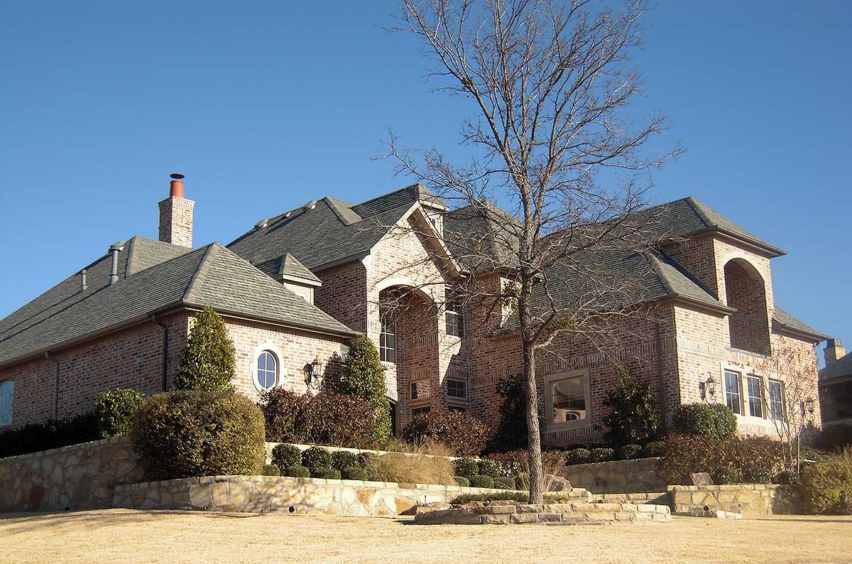 House plan exterior: Two-story brick residence with multiple gables, arched entryway, round dormer window, and a prominent brick chimney.