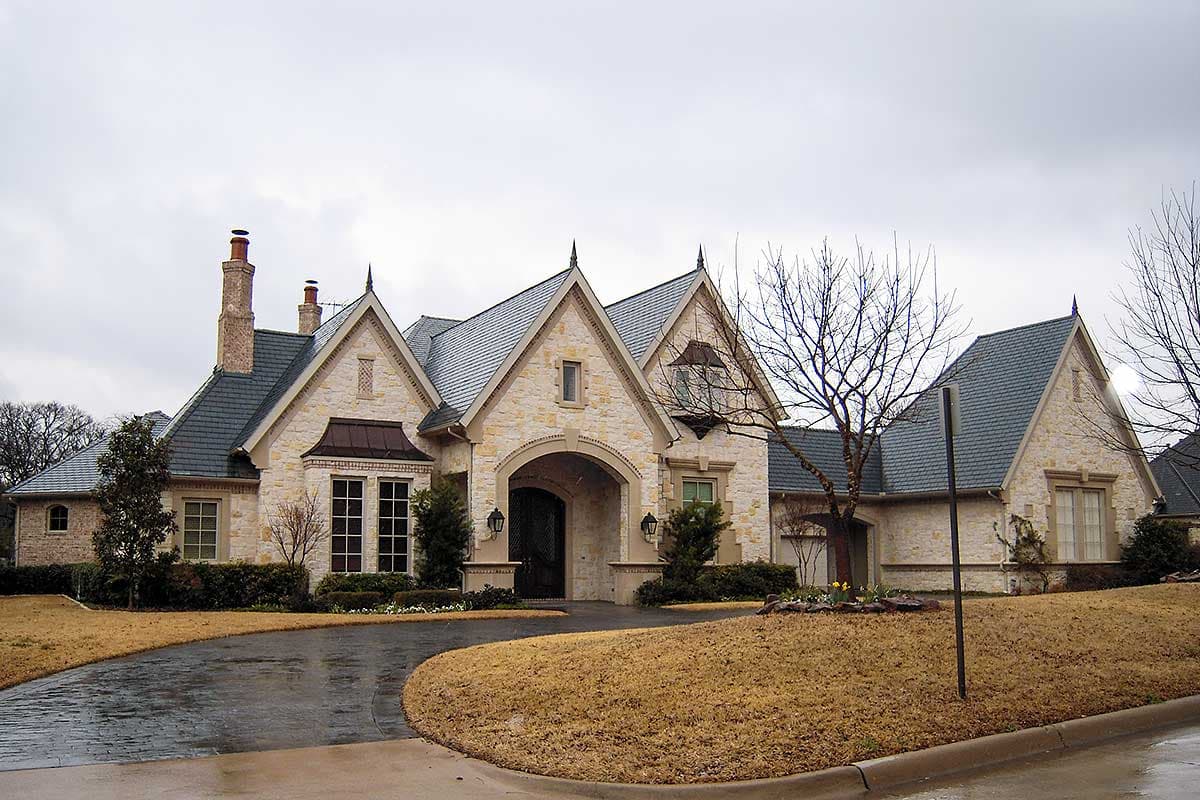 House plan exterior with stone facade, multiple gables, and a slate roof. Features include an arched entryway and dormer windows.