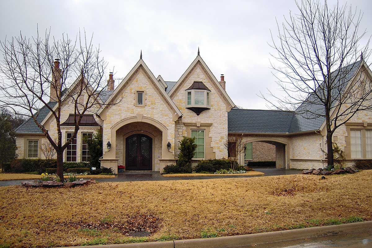 House plan exterior with stone facade, arched entryway, multiple gables, and a porte-cochère.