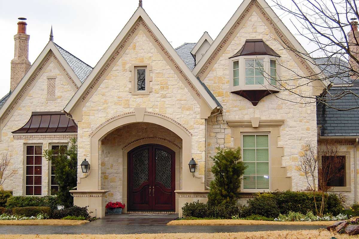 House plan exterior with stone facade, arched entry, double doors, bay window, gables with copper roofs, and chimney.
