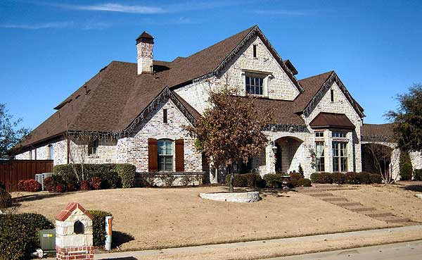 House plan exterior: Two-story home with stone facade, arched entryway, gables, and a prominent brick chimney.