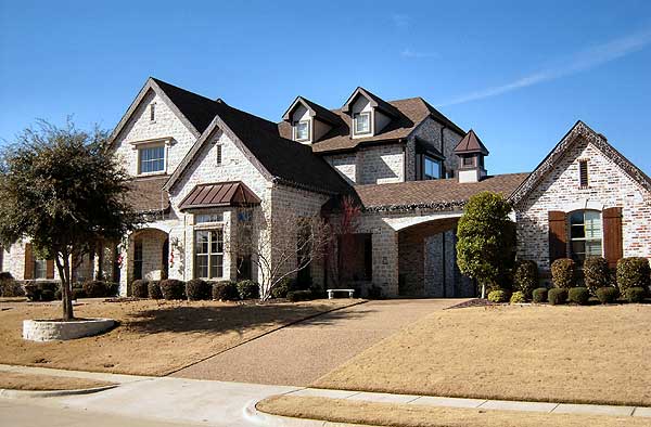 House plan exterior: two-story stone house with multiple gables, dormers, arched carport, and prominent chimney.