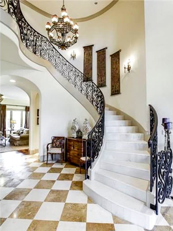 Grand foyer with a sweeping curved staircase, wrought iron railings, checkered marble floors, and a large chandelier.