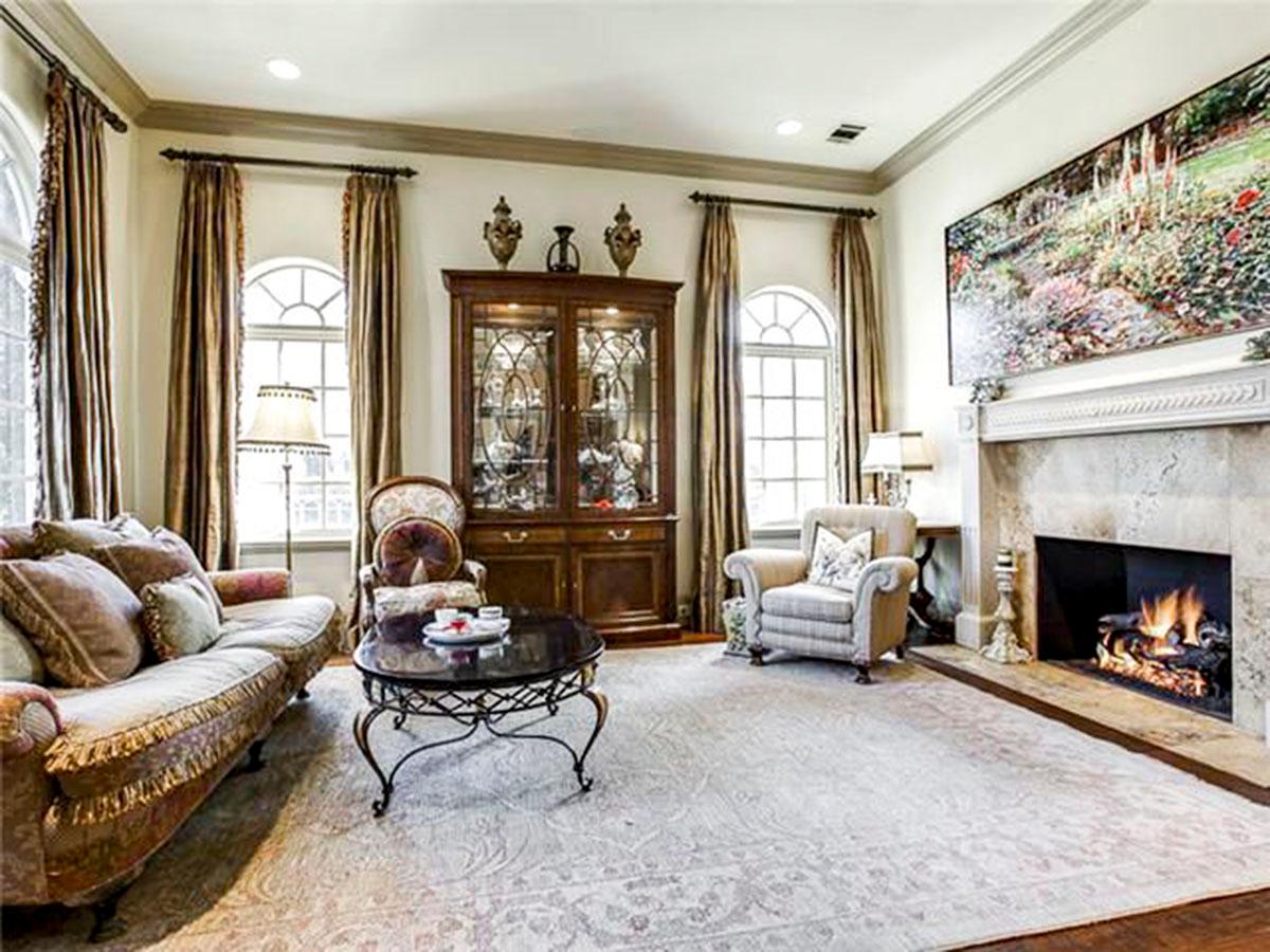 Living room with sofa, armchairs, coffee table, glass cabinet, fireplace, and large landscape painting.