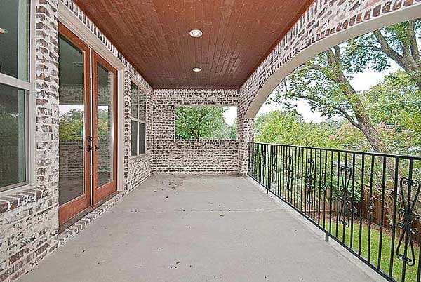 Covered porch with wood ceiling, brick walls, arched opening, decorative metal railing, and double glass doors.