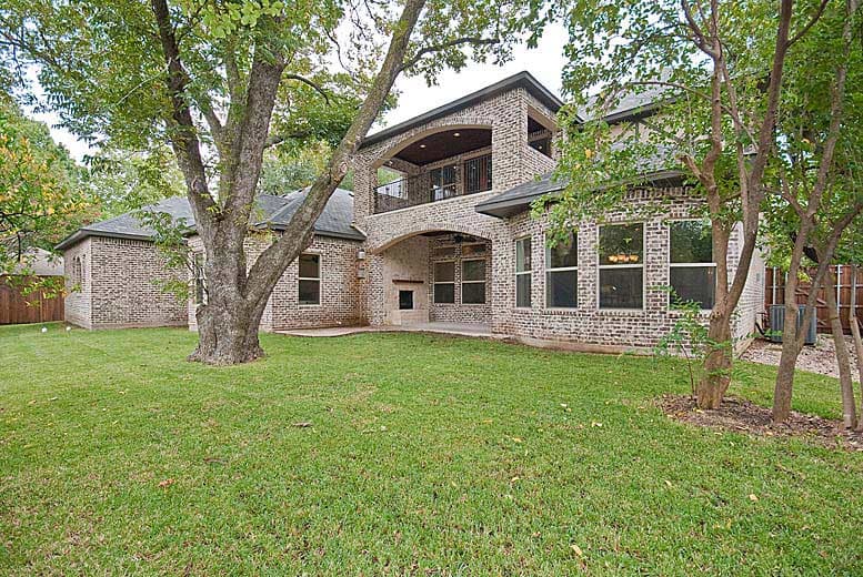 Rear exterior view of a two-story brick house with a covered patio, outdoor fireplace, and second-story balcony.