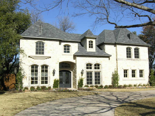 House plan exterior: Two-story home with stone facade, mansard roof, dormers, arched windows, and prominent entry.