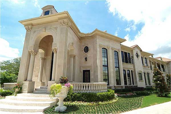 House plan exterior: Large stone mansion with grand arched entryway, multiple stories, and prominent classical columns.