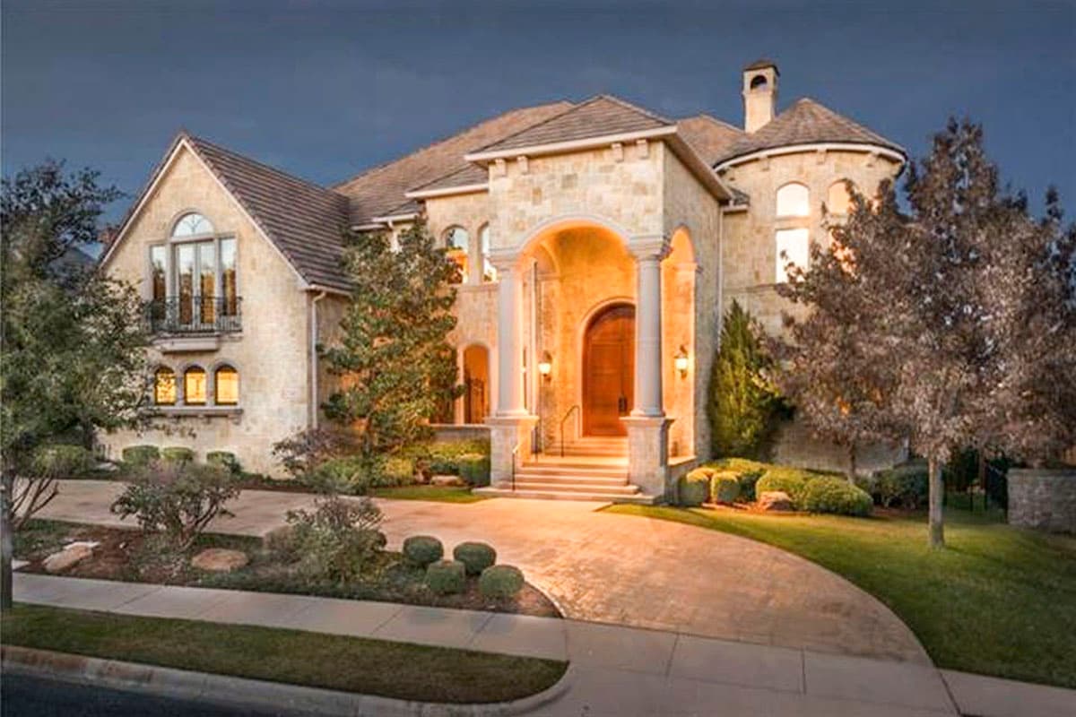 House plan exterior: stone facade, arched entryway with columns, multiple gables, and a turret.