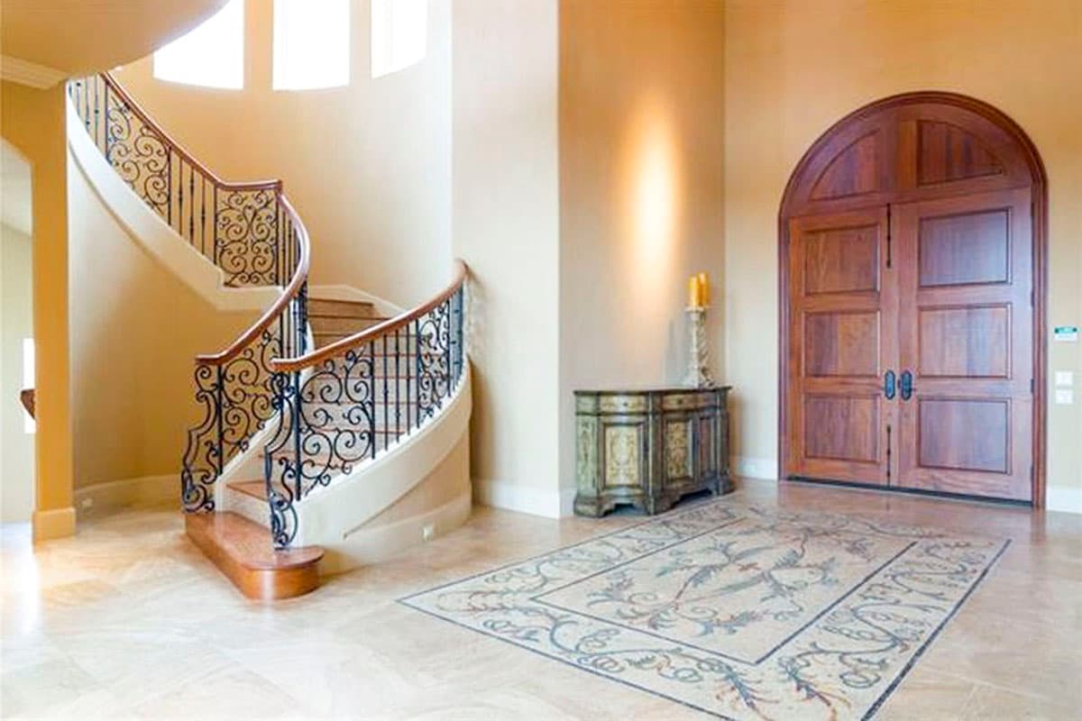 Foyer with spiral staircase featuring ornate metalwork, double wood doors, and mosaic floor inlay.