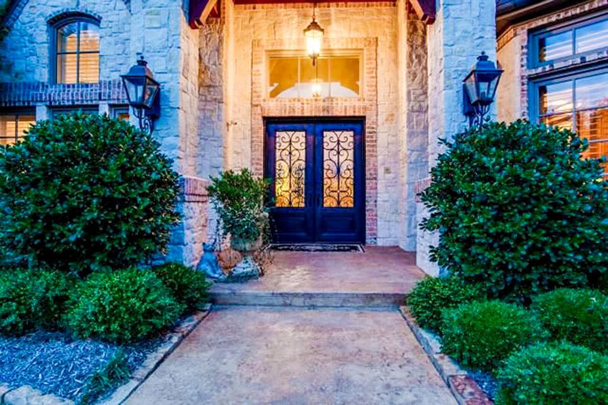 House plan exterior featuring double doors with ornate glass, stone facade, arched window, and lantern sconces.