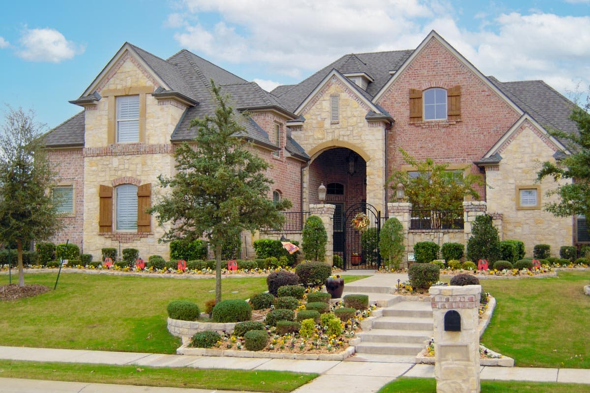 House plan exterior: Two-story brick and stone home with arched entryway, multiple gables, dormers, and decorative shutters.