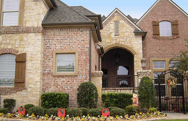 Exterior house plan with brick and stone facade, arched entryway, pitched roof, and decorative shutters.
