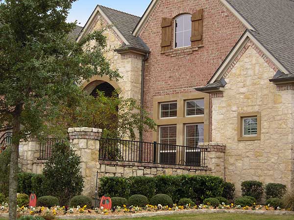 House plan exterior: Traditional brick and stone facade with arched entryway, gables, and multiple windows.