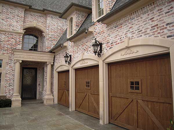 House plan exterior with brick facade, arched entry, three wooden garage doors with small windows, and decorative stone accents.