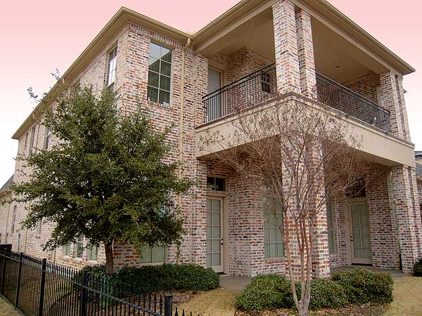 Two-story brick house plan exterior with upper balcony supported by columns, large windows, and multi-pane doors.