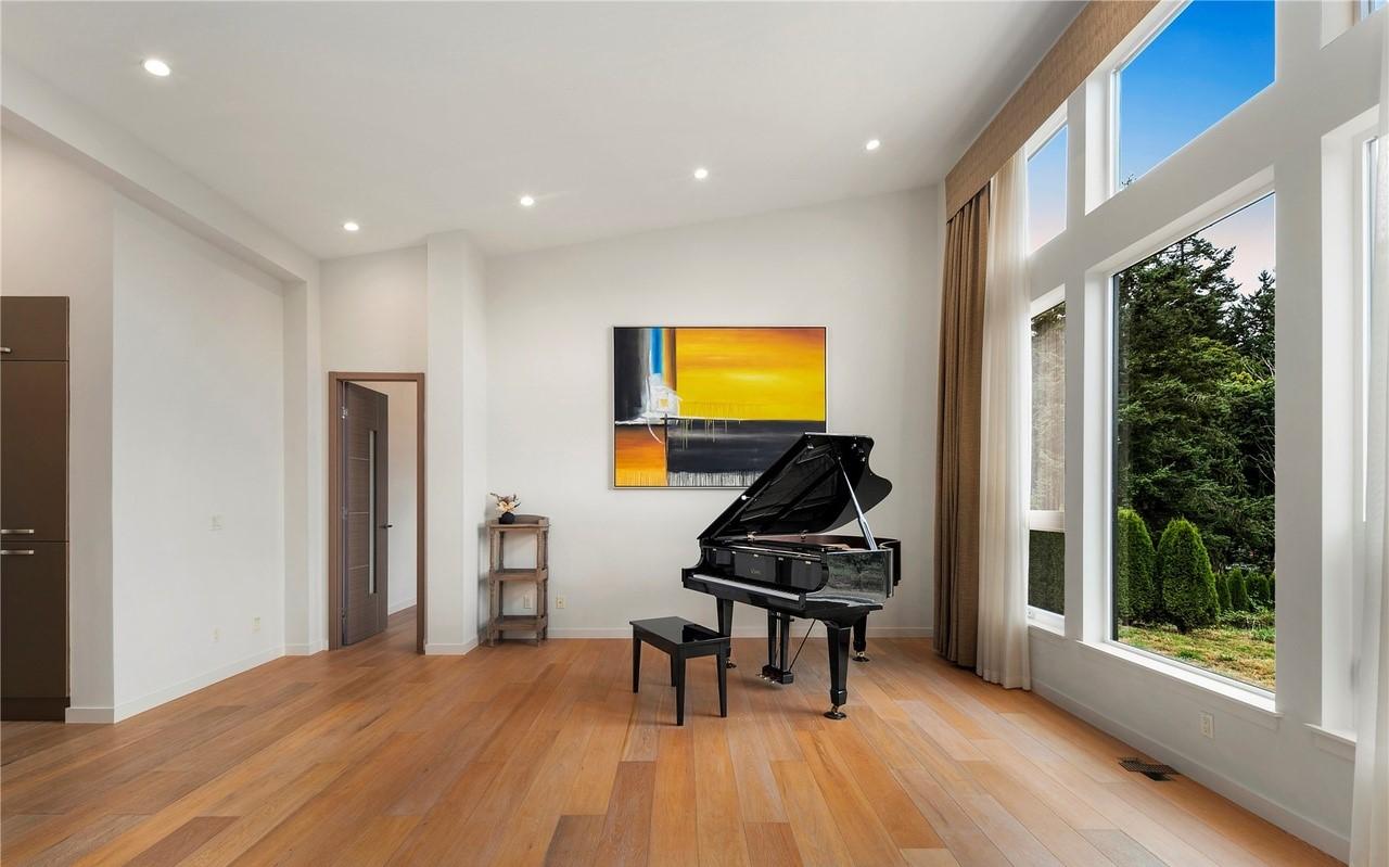 Interior view of a room with a grand piano, large windows, and wood floors. A painting hangs on the wall.