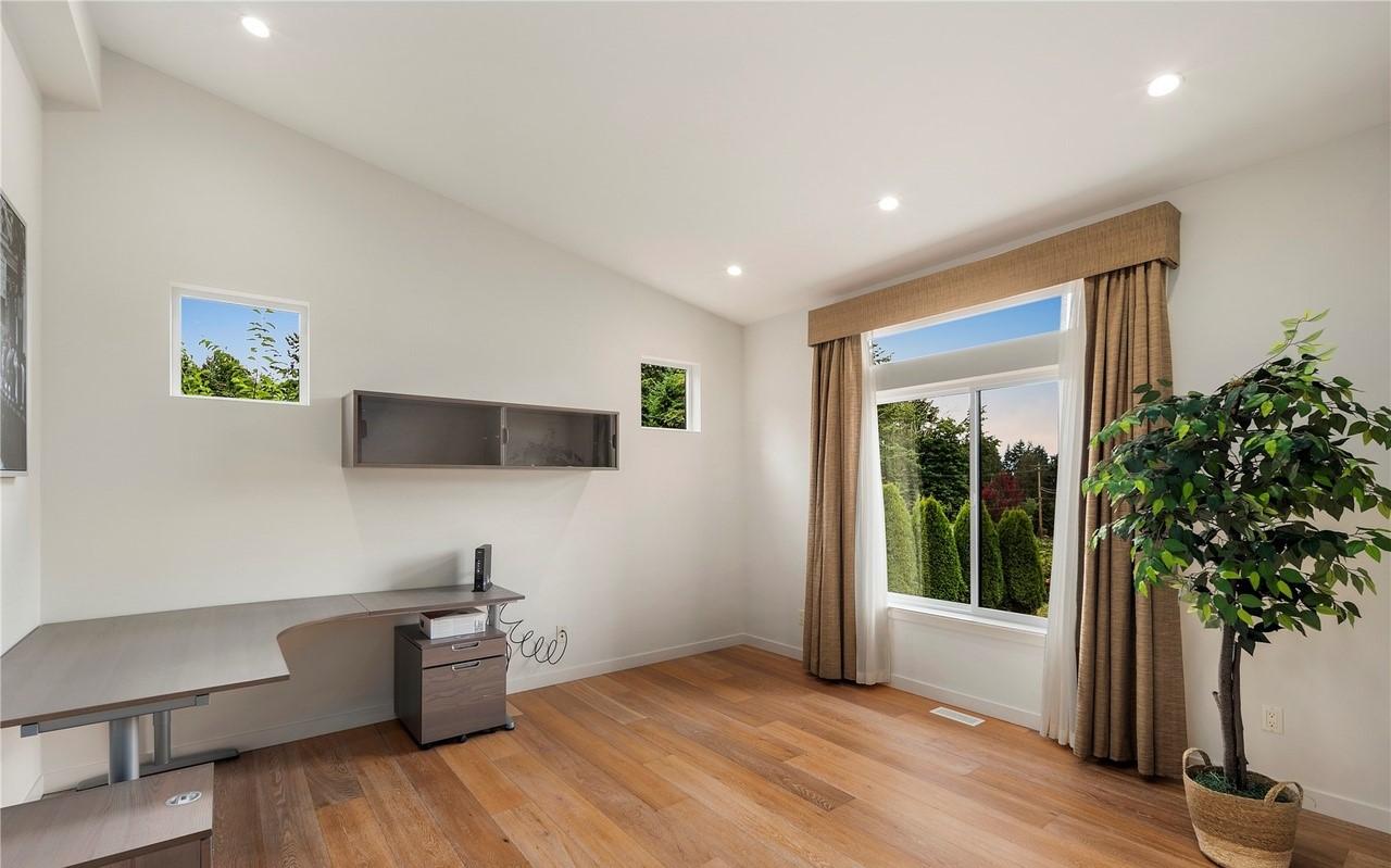 Office with L-shaped desk, floating shelf, and large window overlooking trees.