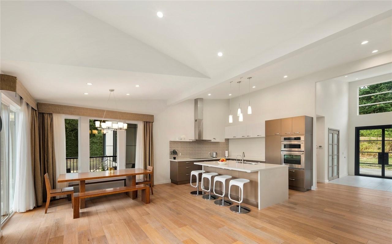 Open concept kitchen and dining area with island, vaulted ceiling, and large windows. Modern design.
