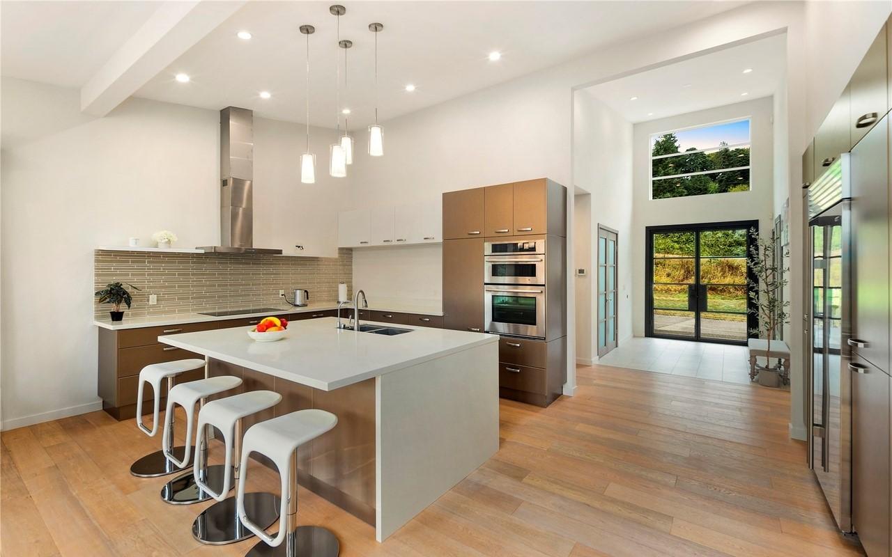 Modern kitchen with island, stainless steel appliances, backsplash, pendant lights, and vaulted ceiling.
