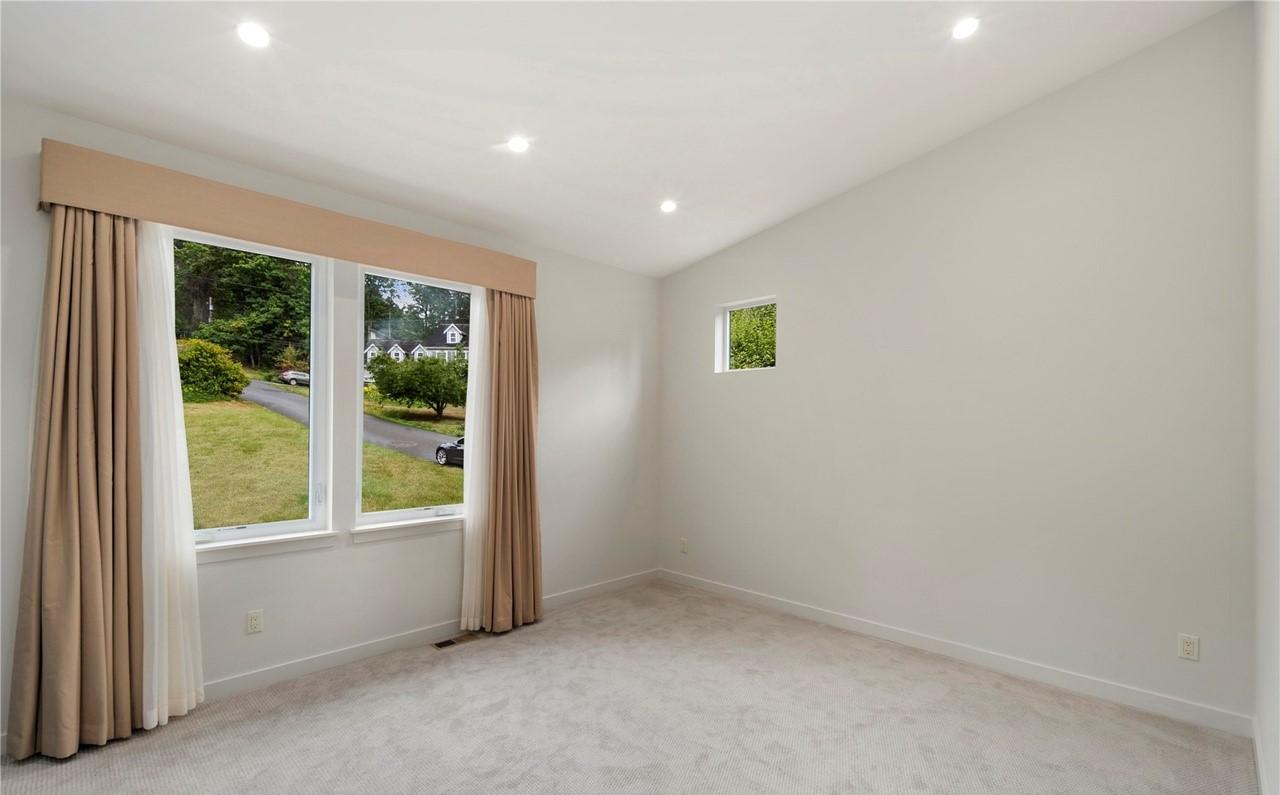Interior view of a room with two large windows, a smaller square window, and carpeted floor.