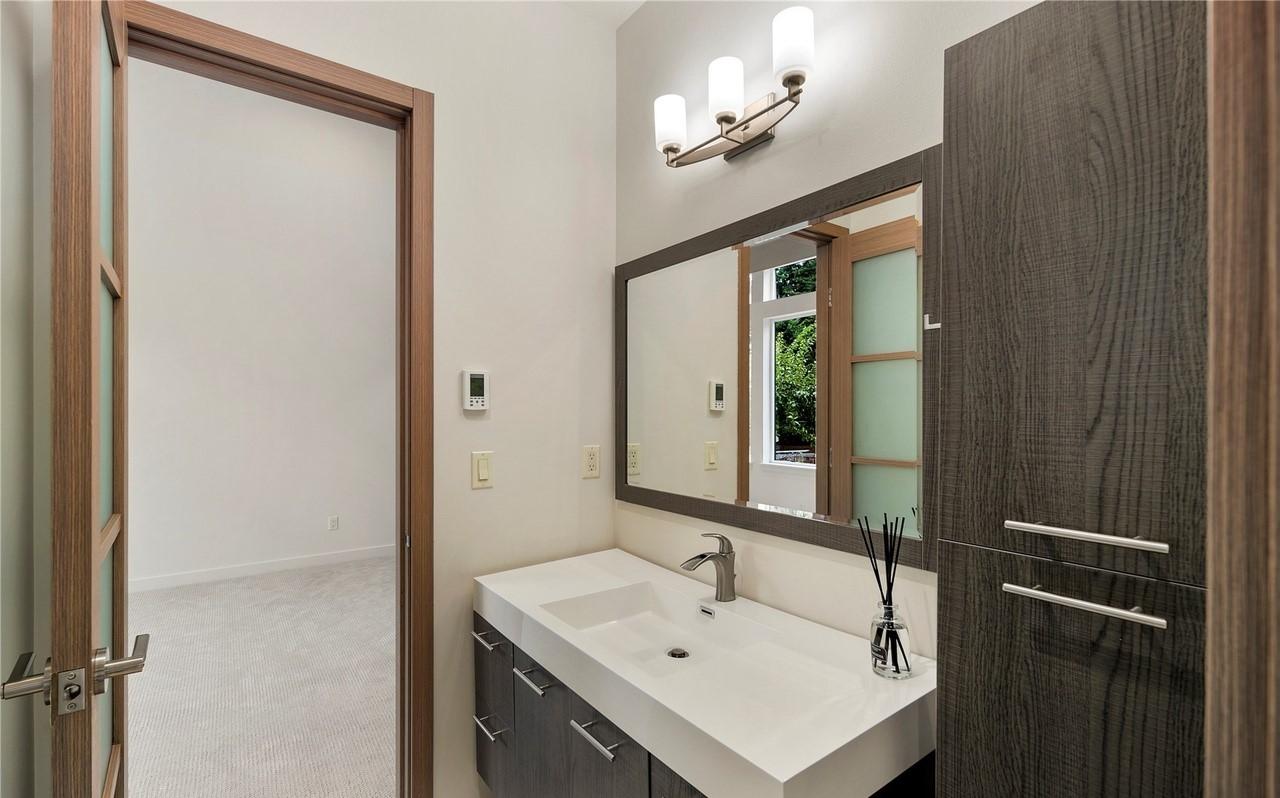 Modern bathroom with floating vanity, integrated sink, and tall wood-grain cabinet. Doorway opens to carpeted room.