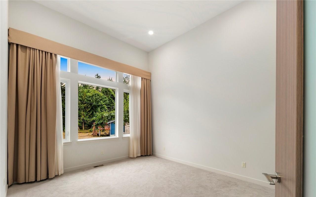 Interior view of room with large corner windows and tan curtains. Neutral carpet and walls. Wood door visible on right.