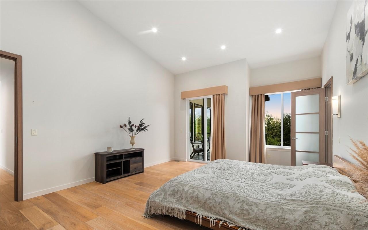 Bedroom interior with vaulted ceiling, hardwood floors, two doors to the exterior, and a media console.