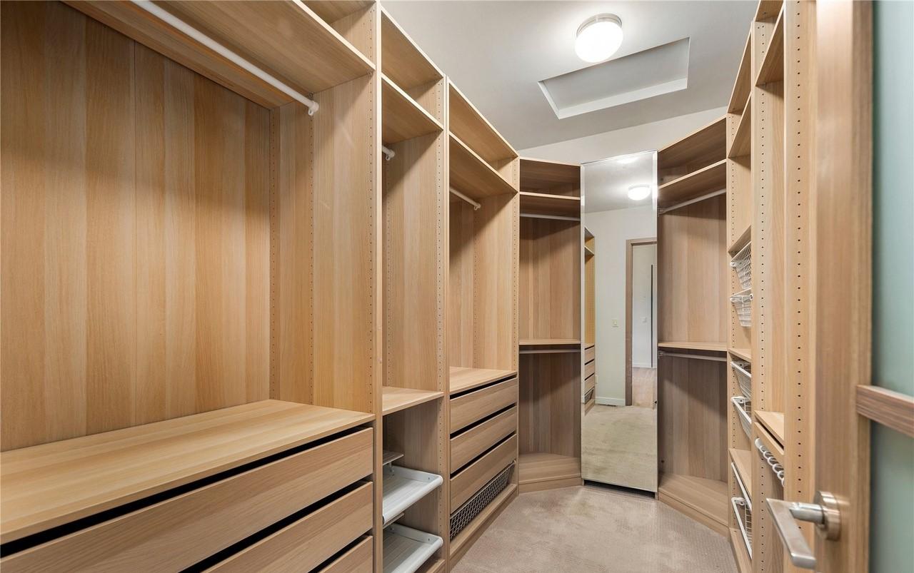 Walk-in closet with built-in wood shelving, drawers, hanging rods, and mirrored wall section.