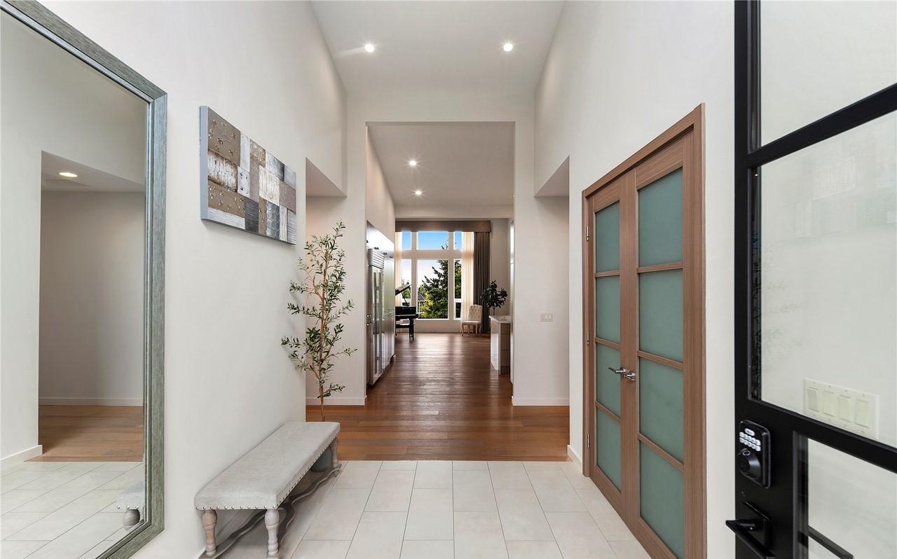 Interior hallway with wood floors, vaulted ceiling, natural light, double doors, and a bench.
