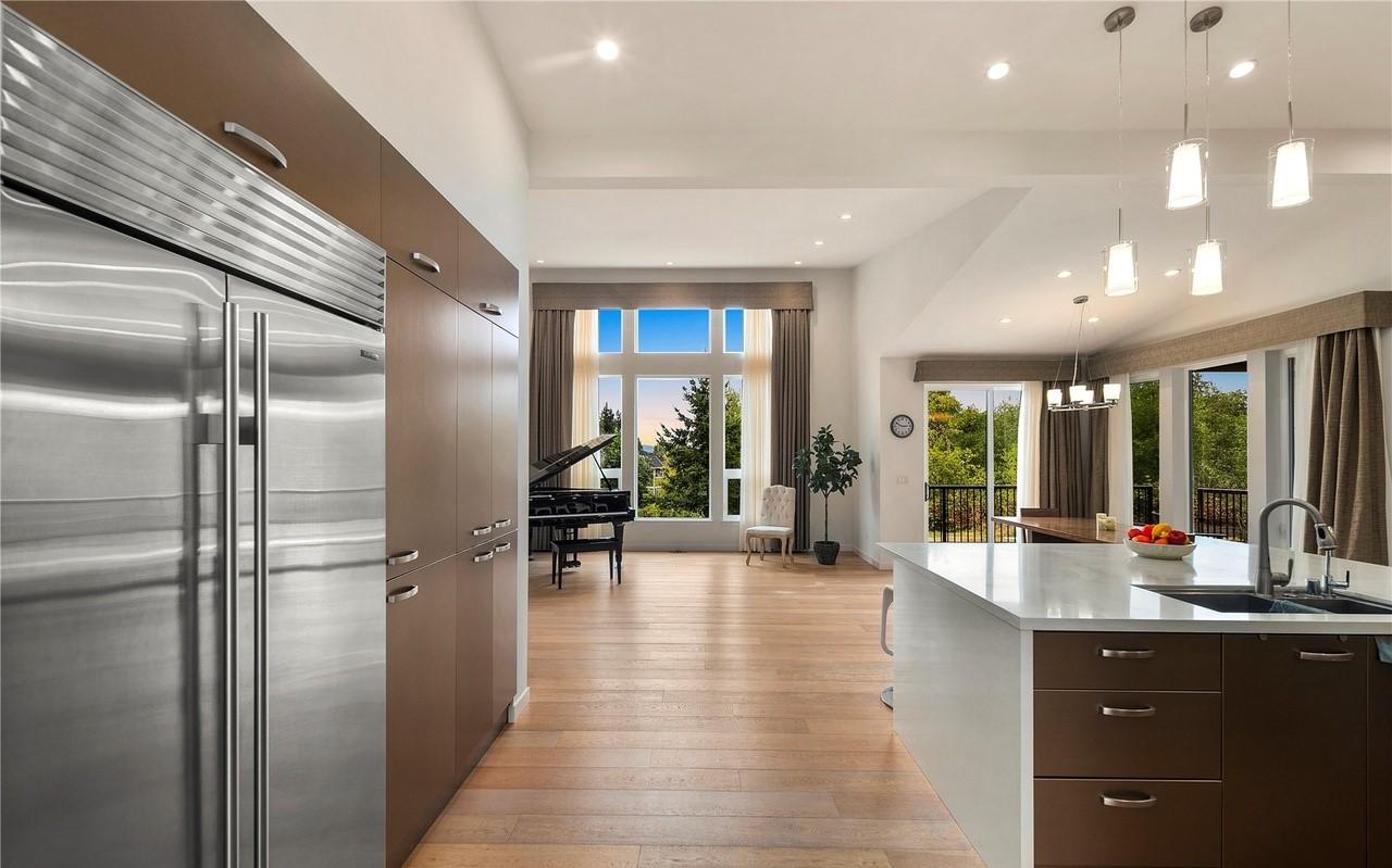 Open concept living area with large windows, a piano, kitchen island, and dining space with balcony access.