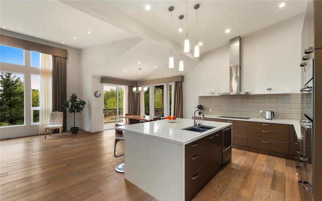 Modern kitchen with island, stainless steel appliances, vaulted ceiling, and large windows overlooking trees.