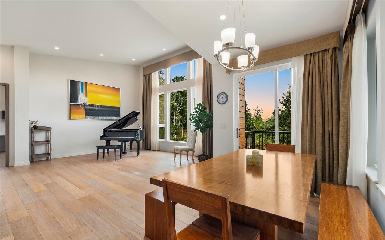 Open-concept dining and living area with grand piano, large windows, and balcony access.