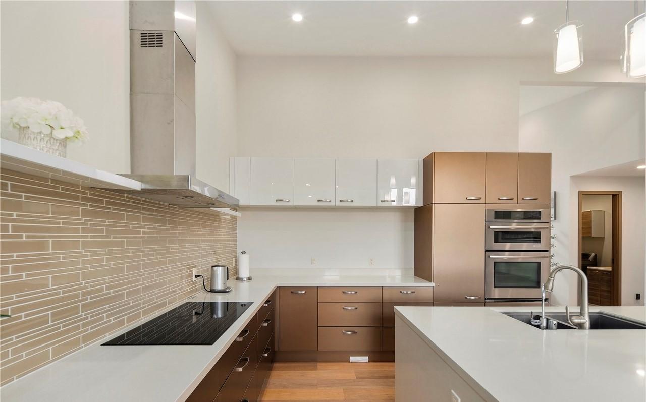Modern kitchen with stainless steel range hood, two-tone cabinets, built-in ovens, and a large island with sink.