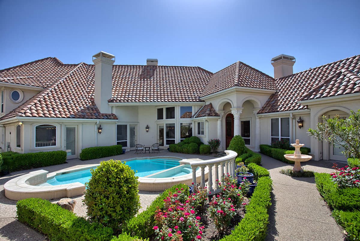 House plan exterior. Two-story Mediterranean style with tile roof, arched entryway, and a pool. Includes manicured landscaping with a fountain.