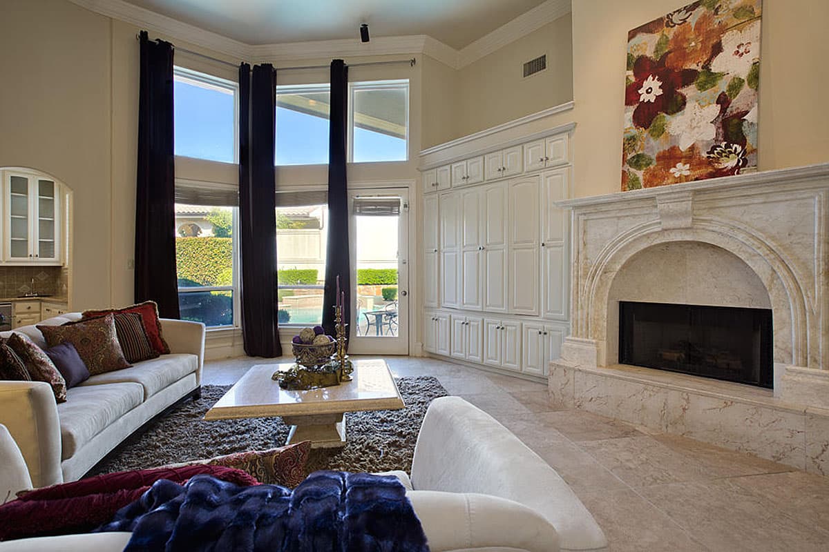 Interior view of living room with fireplace, built-in cabinets, and large windows overlooking a pool and patio.
